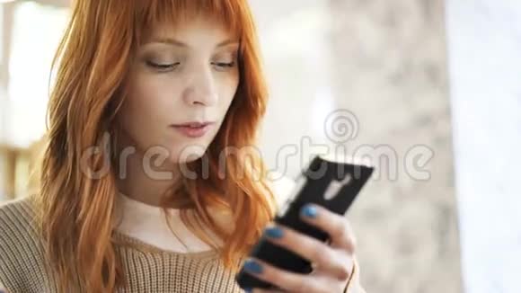 红头发的女人用智能手机上网和阅读视频的预览图