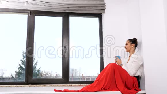 一个女人坐在一扇大窗户旁边身披红毯视频的预览图