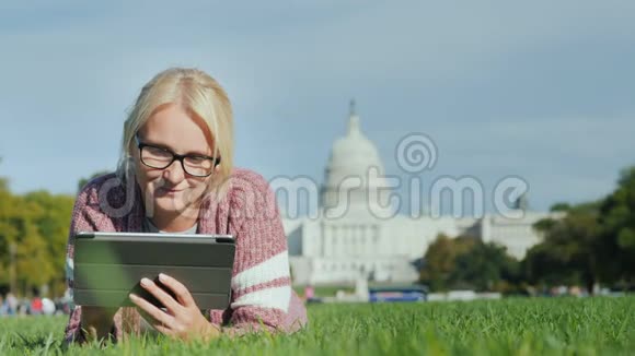 一位女士躺在华盛顿国会大厦背景下的草坪上使用平板电脑旅游学习和旅行视频的预览图