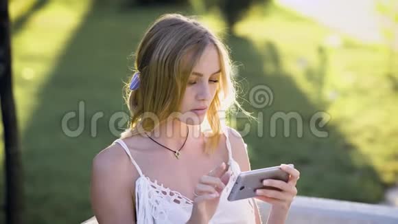 穿着白色连衣裙的漂亮女孩手持手机通过新闻提要上网的画像视频的预览图