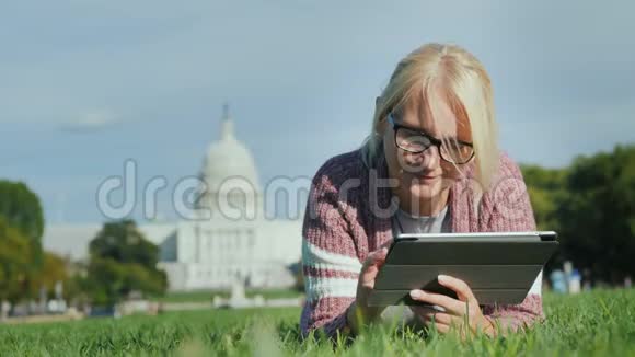 一位女士躺在华盛顿国会大厦背景下的草坪上使用平板电脑旅游学习和旅行视频的预览图
