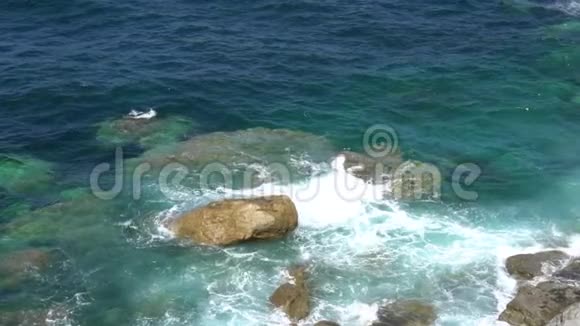 在晴朗晴朗的天气里泡沫的波浪在岩石海岸上破浪前进视频的预览图
