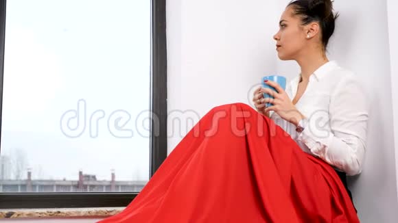 一个女人坐在一扇大窗户旁边身披红毯视频的预览图