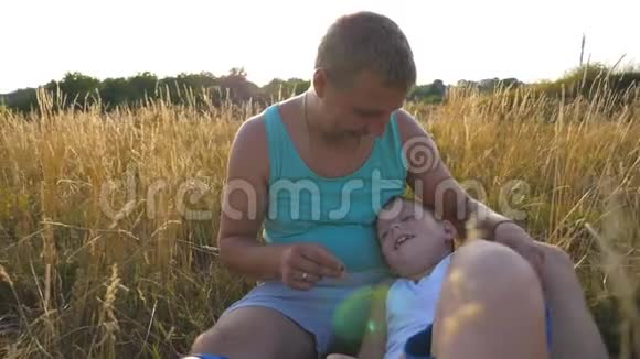 快乐的年轻人坐在草地上和他的小男孩玩快乐的爸爸和他的孩子玩得开心视频的预览图