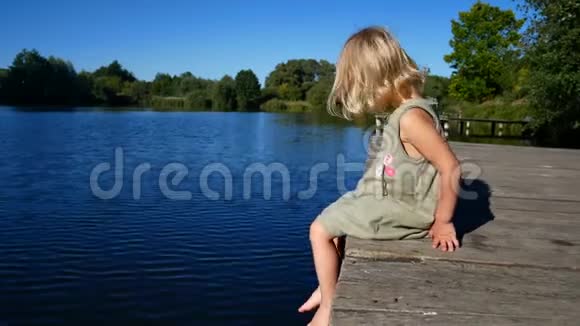 女孩坐在码头上用脚聊天在水边的木桥上的孩子视频的预览图
