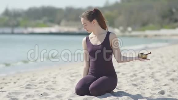 阳光明媚的一天年轻漂亮的女人在海滩上练习瑜伽女人用藏式唱碗冥想视频的预览图