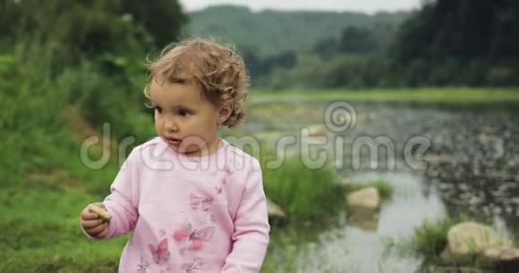 金发卷曲的小女孩在河里扔石头山脉背景视频的预览图