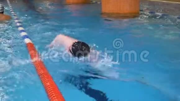 年轻人带着护目镜和帽子在游泳池的蓝色水中游泳室内运动员在清澈的海水中游泳视频的预览图