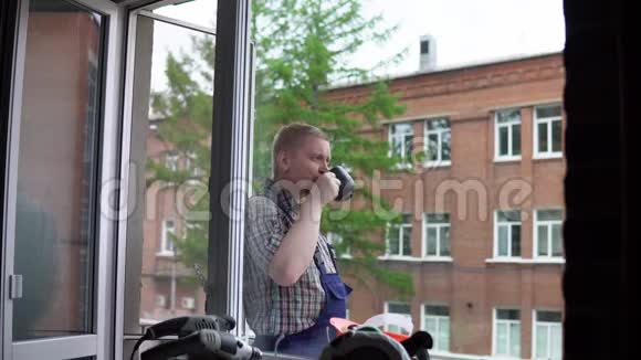 一个工人喝一杯黑杯子里的热饮料对着一座砖楼视频的预览图