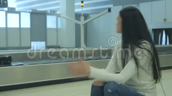 年轻的黑发女人紧张地在机场等她的行李视频的预览图