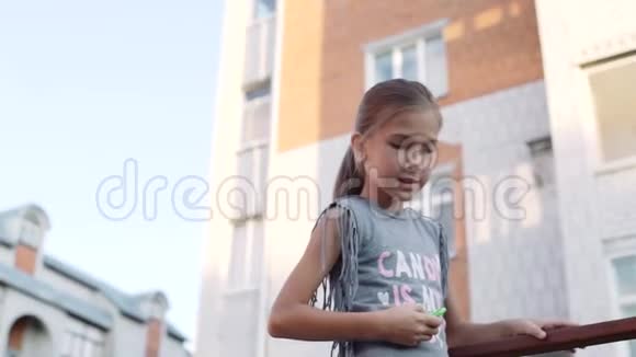 一个手里拿着旋转器的小女孩站在一栋多层建筑的背景上日落视频的预览图