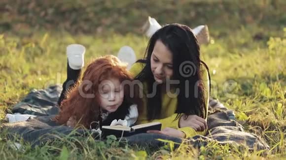 美丽的妈妈和她可爱的小女儿躺在公园的草地上看书他们说得很好快乐视频的预览图