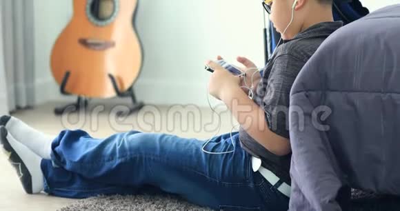 带智能手机和耳机的亚洲男孩在家听音乐或玩游戏视频的预览图