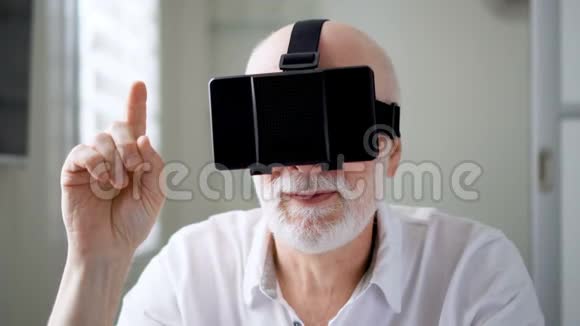 英俊的白人老人在家里使用VR360眼镜进行浏览缩放和点击手势视频的预览图