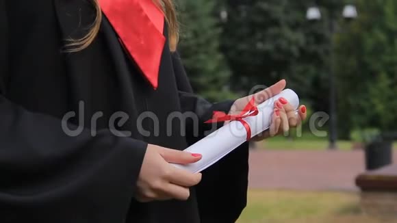 年轻女子穿着学术服装拿着文凭享受毕业典礼视频的预览图