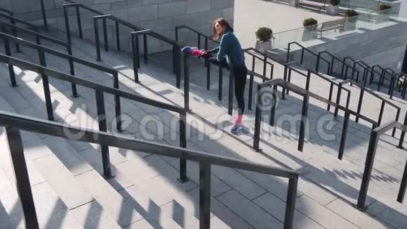 在城市体育场的楼梯上积极运动的女孩做腿部热身运动的高角度视图年轻女性视频的预览图