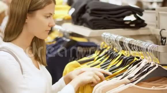 女人在商场购物站在货架附近衣服选择套头衫捡起黄色的球衣视频的预览图