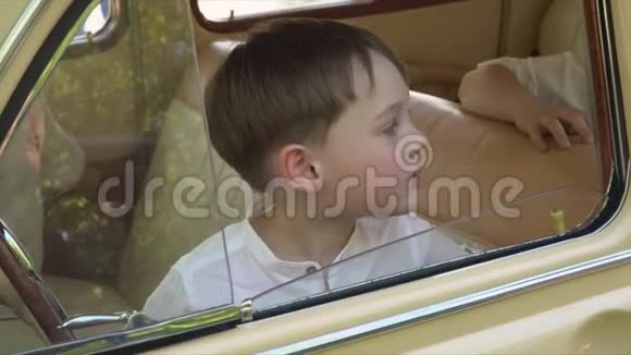 这个小男孩想着坐在复古车里的轮子和窗户前视频的预览图