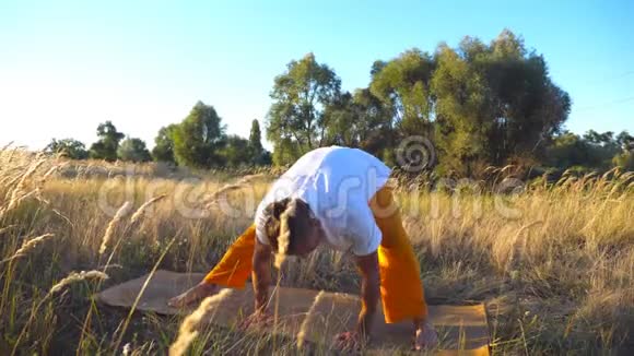 在球场上练习瑜伽动作和在垫子上的位置的运动型家伙在草地上做运动的年轻人视频的预览图