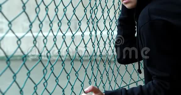 戴着头巾站在栅栏附近的悲伤女学生的肖像视频的预览图