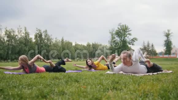 公园的户外瑜伽训练男子和两个漂亮的健身模特表演练习视频的预览图