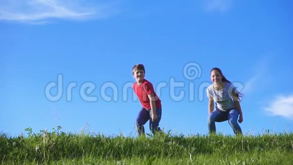 快乐的孩子们在蓝天的绿色草地上跳跃视频的预览图