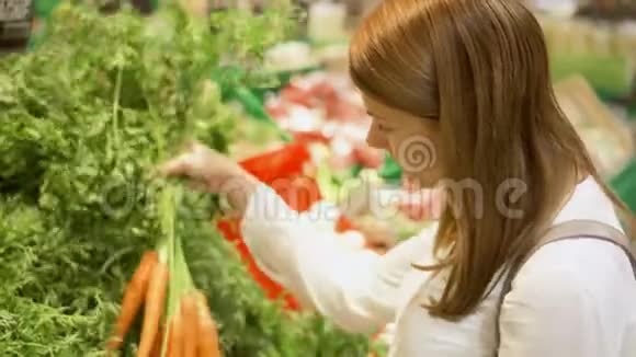 年轻女子在杂货店购物站在蔬菜部挑选新鲜胡萝卜视频的预览图