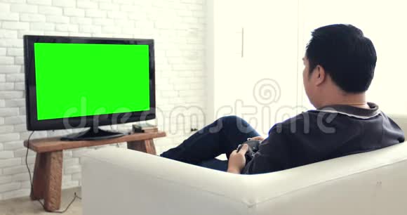 亚洲男人玩电脑游戏用绿色屏幕在电视上视频的预览图