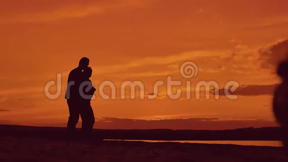 日落时分一对夫妇在海滩上牵手散步的剪影在夕阳的灯光下在海滨快乐的男人和女孩视频的预览图