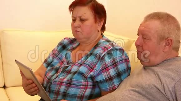 成熟的夫妻坐在沙发上用平板电脑视频的预览图