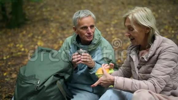 快乐的老年夫妇在树林里享用他们的旅游午餐视频的预览图