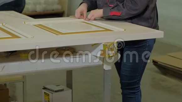 在一家工厂一名妇女用一条保护胶带把室内木门的生产贴在门上视频的预览图