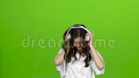 女孩耳朵里戴着耳机在不同的方向挥舞着头她喜欢音乐绿色屏幕慢动作视频的预览图