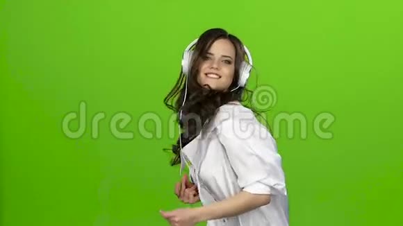 戴着耳机的女孩在舞蹈中旋转她喜欢音乐绿色屏幕慢动作视频的预览图