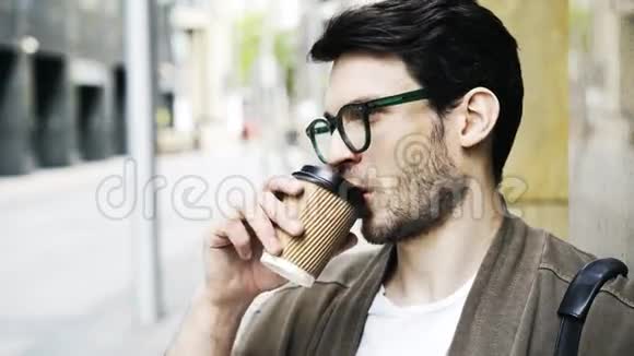 戴眼镜喝咖啡在街边特写镜头前等待的英俊青年视频的预览图