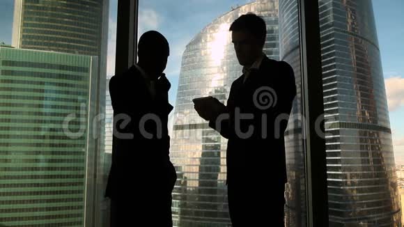 两位多元文化的男性同事正在讨论项目站在办公室的窗户旁视频的预览图