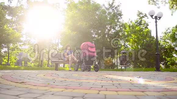 美丽的年轻妈妈吃冰淇淋在公园里和婴儿车散步暑假全家放假视频的预览图