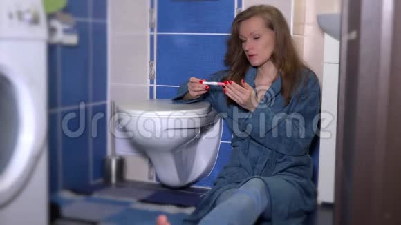 穿着睡衣看着怀孕测试的悲伤女人坐在浴室的壁橱附近视频的预览图