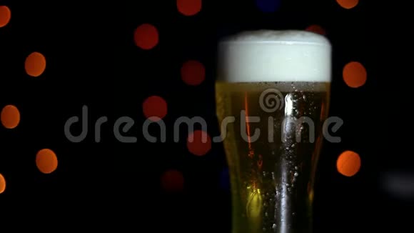 酒吧里有一杯黑色背景上的冷啤酒上面有彩灯啤酒在玻璃杯里起泡视频的预览图