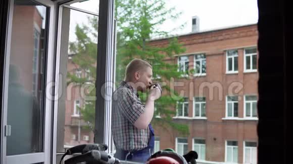 一个工人喝一杯黑杯子里的热饮料对着一座砖楼视频的预览图
