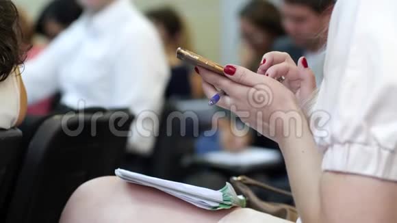 带着记事本的女孩坐在会议室里滚动屏幕女性手的特写正在输入短信视频的预览图