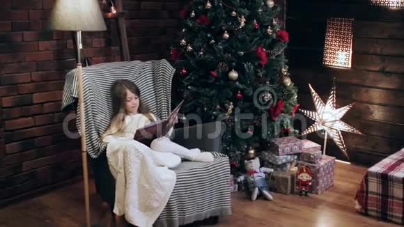 一个小女孩在家中的圣诞树附近看书视频的预览图