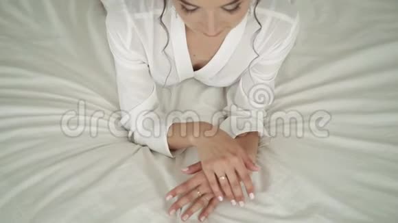 女孩躺在床上摸着她的手白色床上的女孩新娘正在抚摸她的手视频的预览图