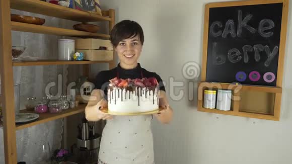 穿着围裙的年轻美女在厨房用奶油和浆果做蛋糕视频的预览图