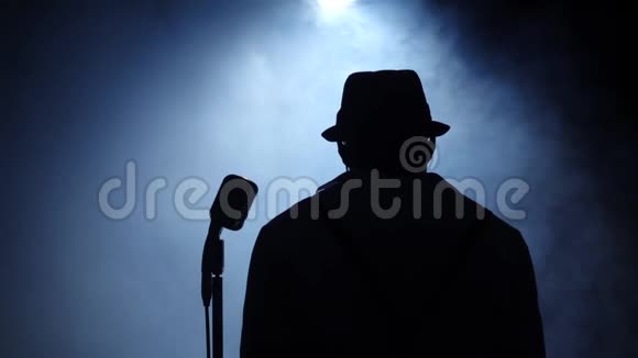 歌手在麦克风在烟雾和白光唱歌黑色背景剪影慢动作关门视频的预览图