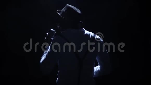 艺术家戴着帽子微弱的灯光在麦克风上唱着这首歌黑色背景剪影慢动作关门视频的预览图