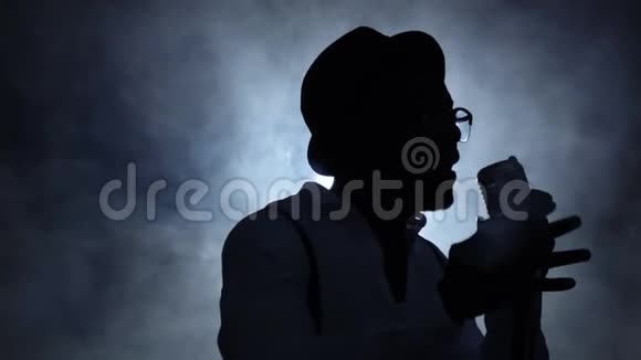 男人一半的营业额在烟雾和白光唱着麦克风黑色背景剪影慢慢视频的预览图