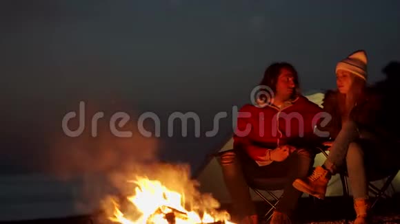 一对年轻夫妇坐在火炉旁在海边用帐篷露营春天视频的预览图