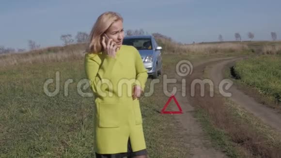 迷人的商务女性通过手机呼救女孩在农村公路上的破车附近慢动作视频的预览图