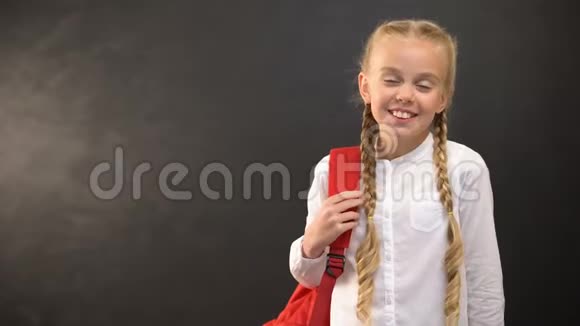 带着背包的微笑女孩在黑板背景上的摄像机上微笑教育视频的预览图